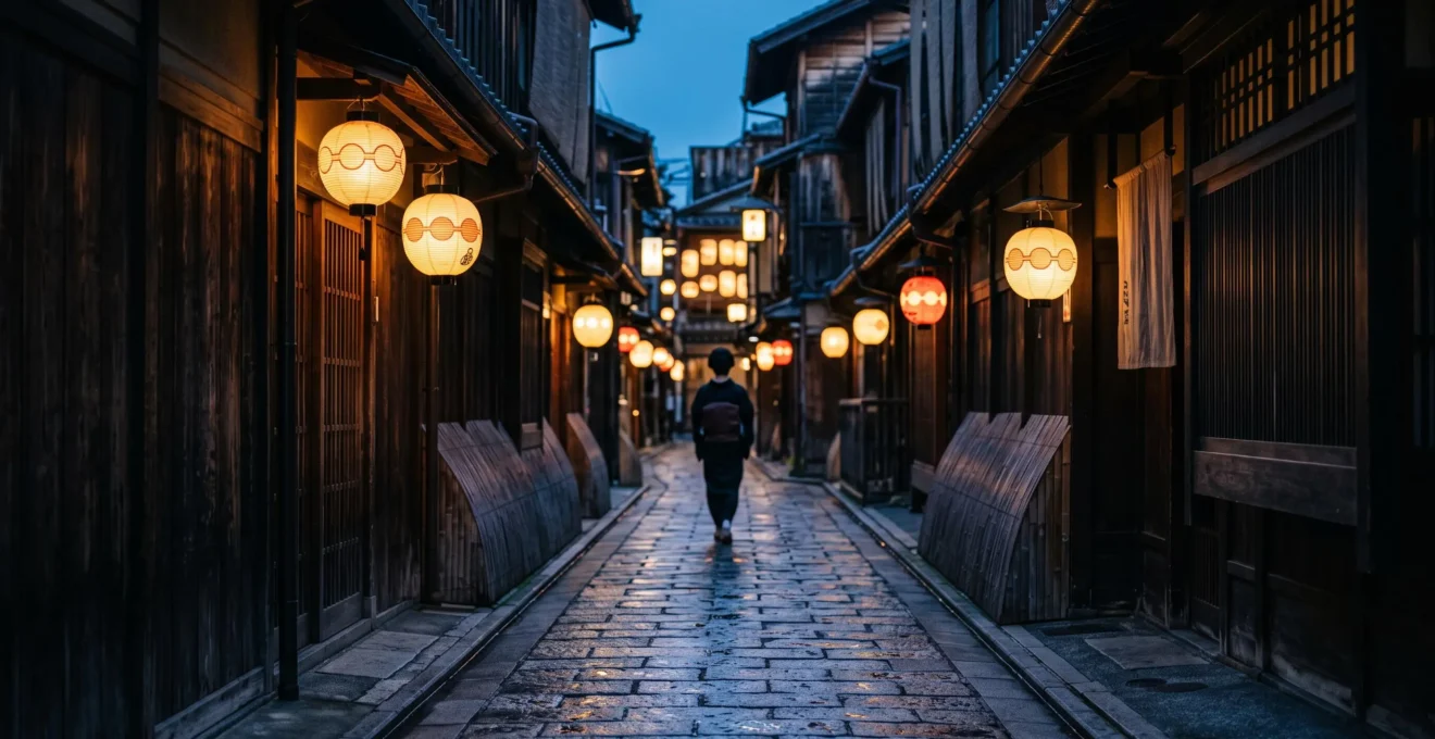 Ruelle pavee du quartier de Gion a Kyoto au crepuscule, lanternes allumees et silhouette discrete en kimono au loin